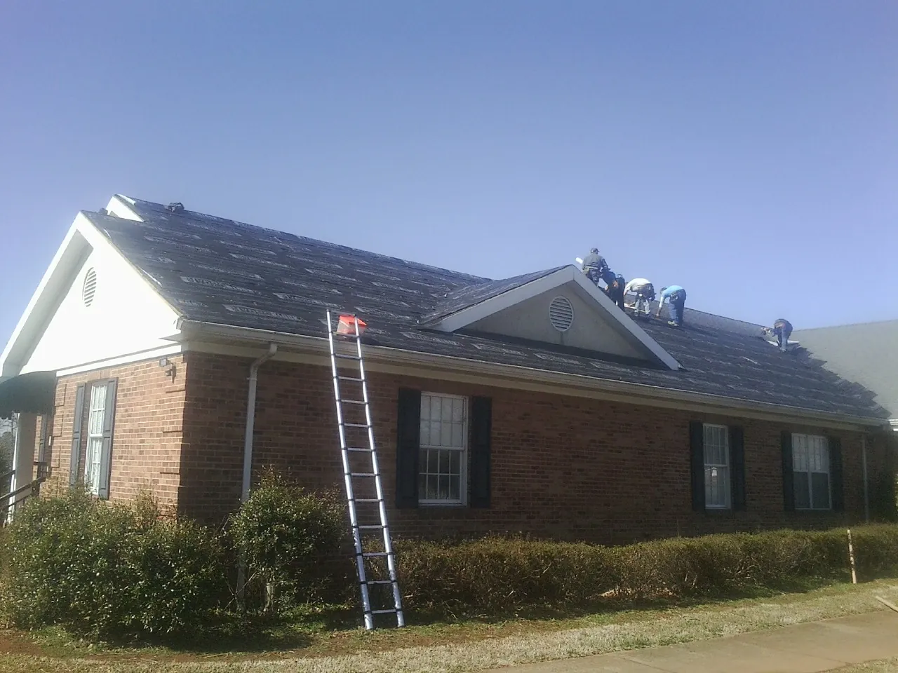 Crew tearing shingles off a brick ranch roof with a ladder set — Emergency Roof Repair work by our crew in Dublin