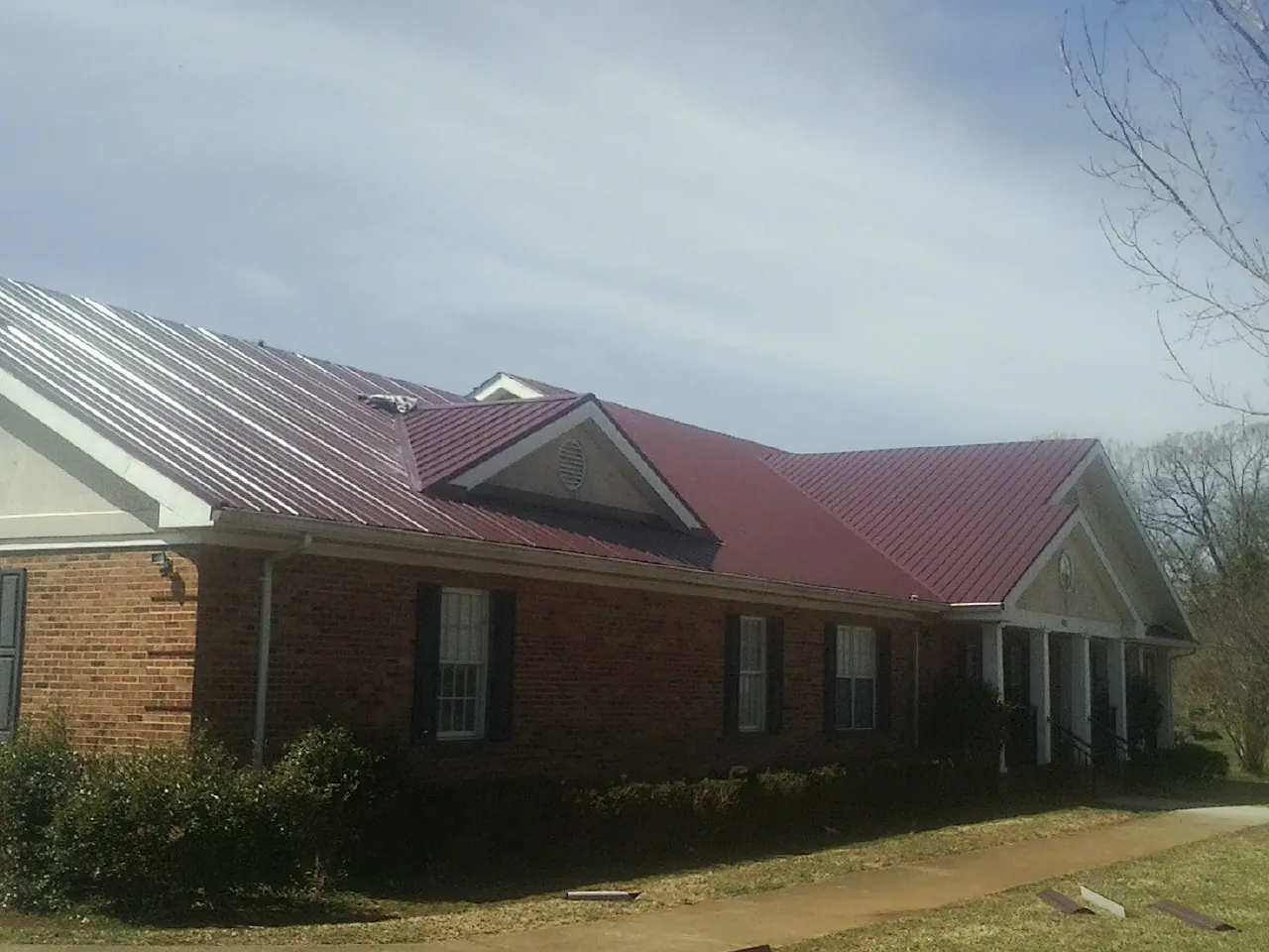 Red metal roof with gabled entries on a long brick building, from a Hail Damage Roof Repair job in Dublin